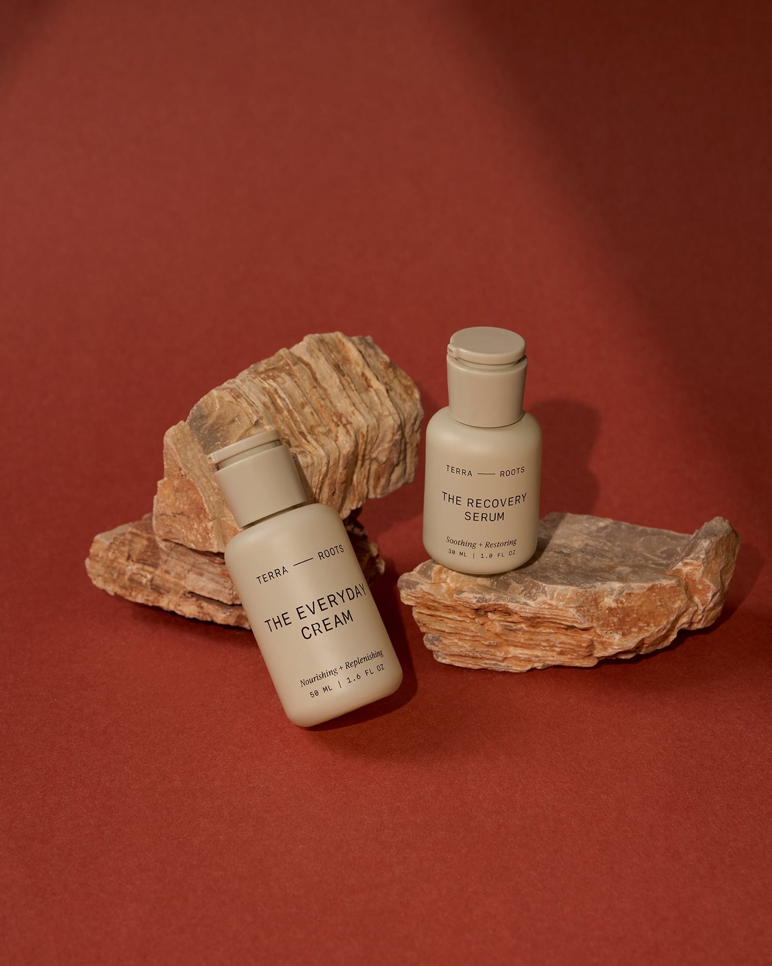 Two skincare bottles on natural stone surfaces against a red background