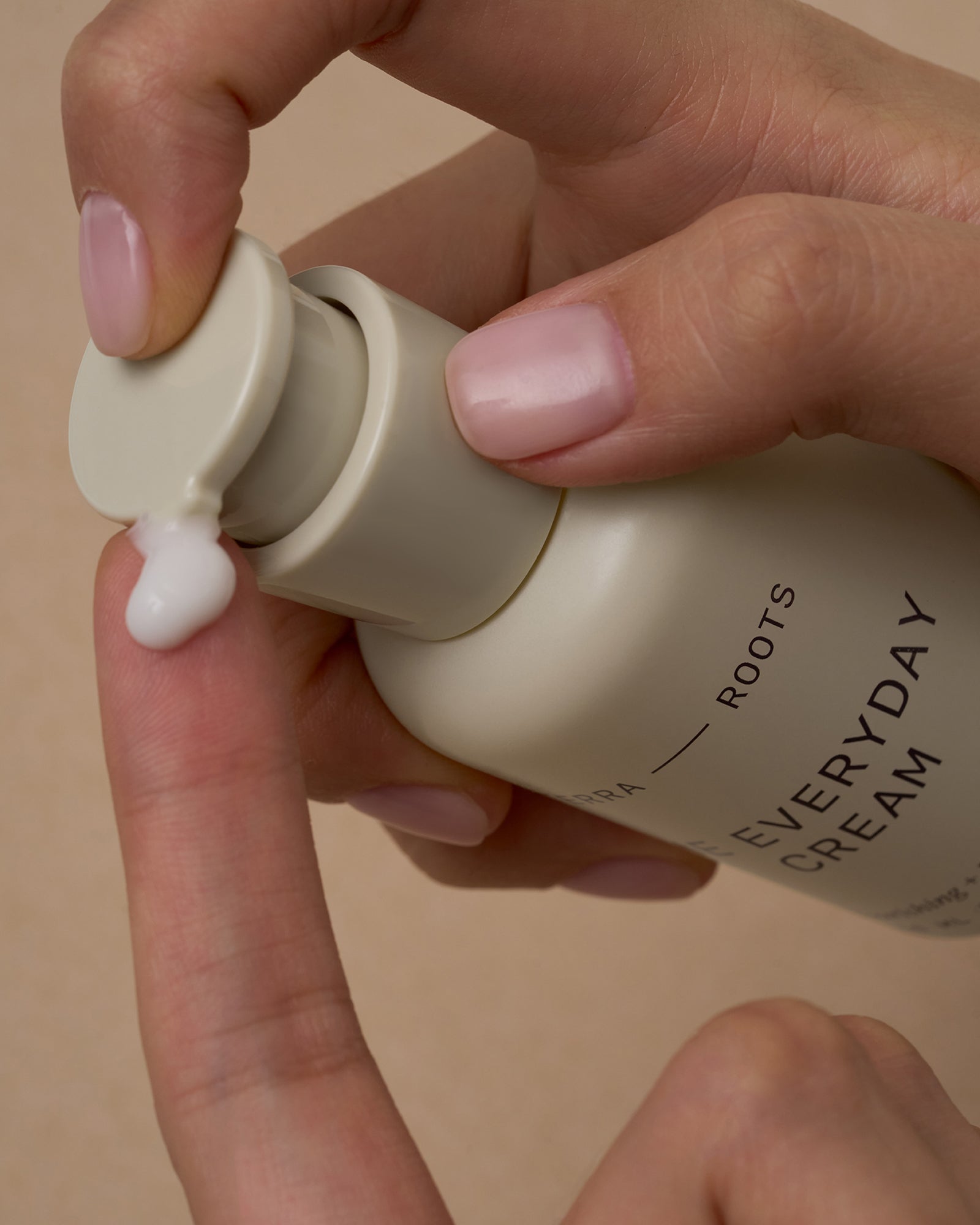 Hand applying cream from a bottle labeled 'Everyday Cream' on a beige background