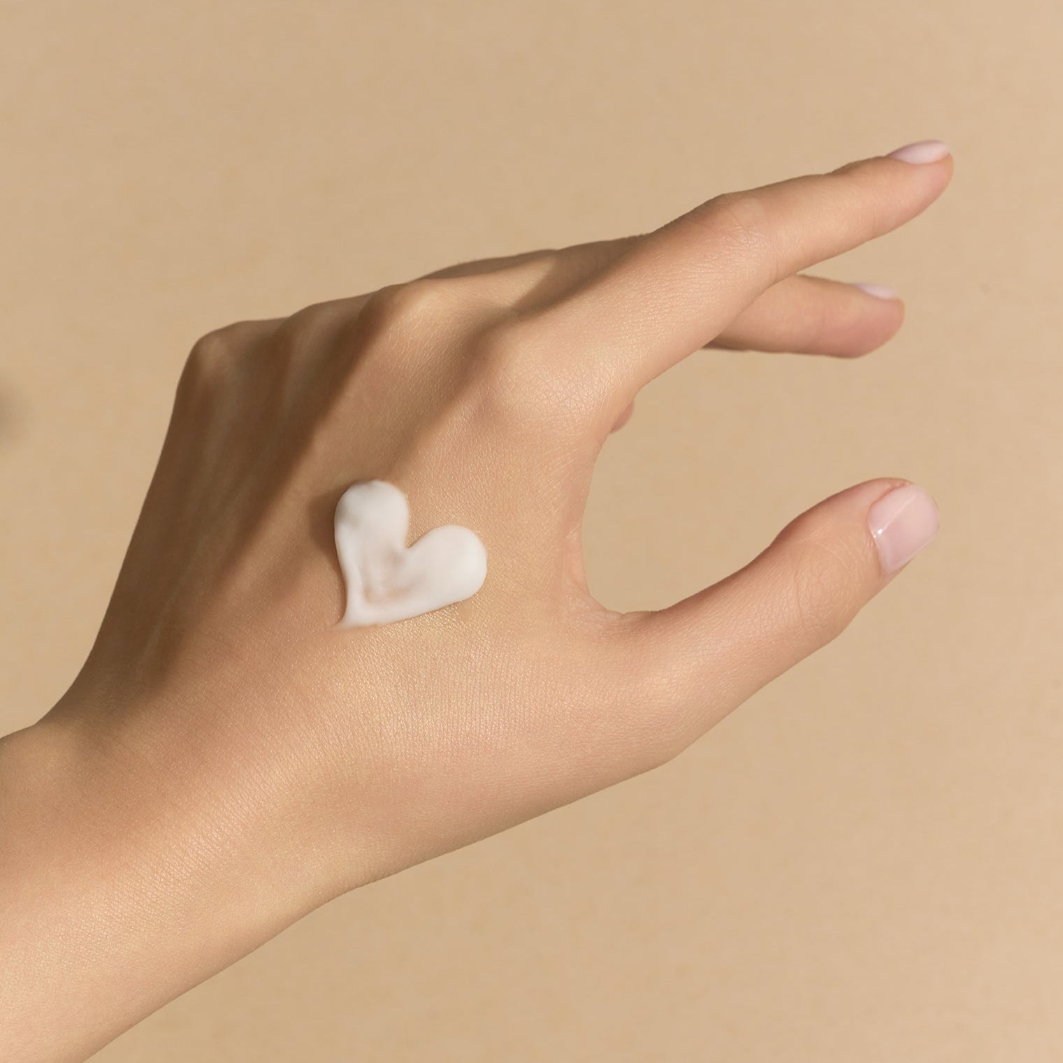Hand with a heart-shaped cream smear on a beige background
