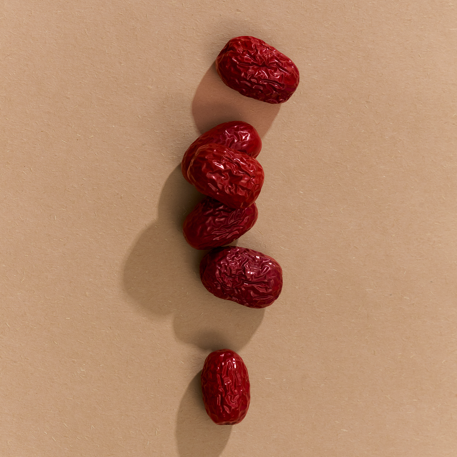 Five red jujubes arranged in a vertical line on a beige background