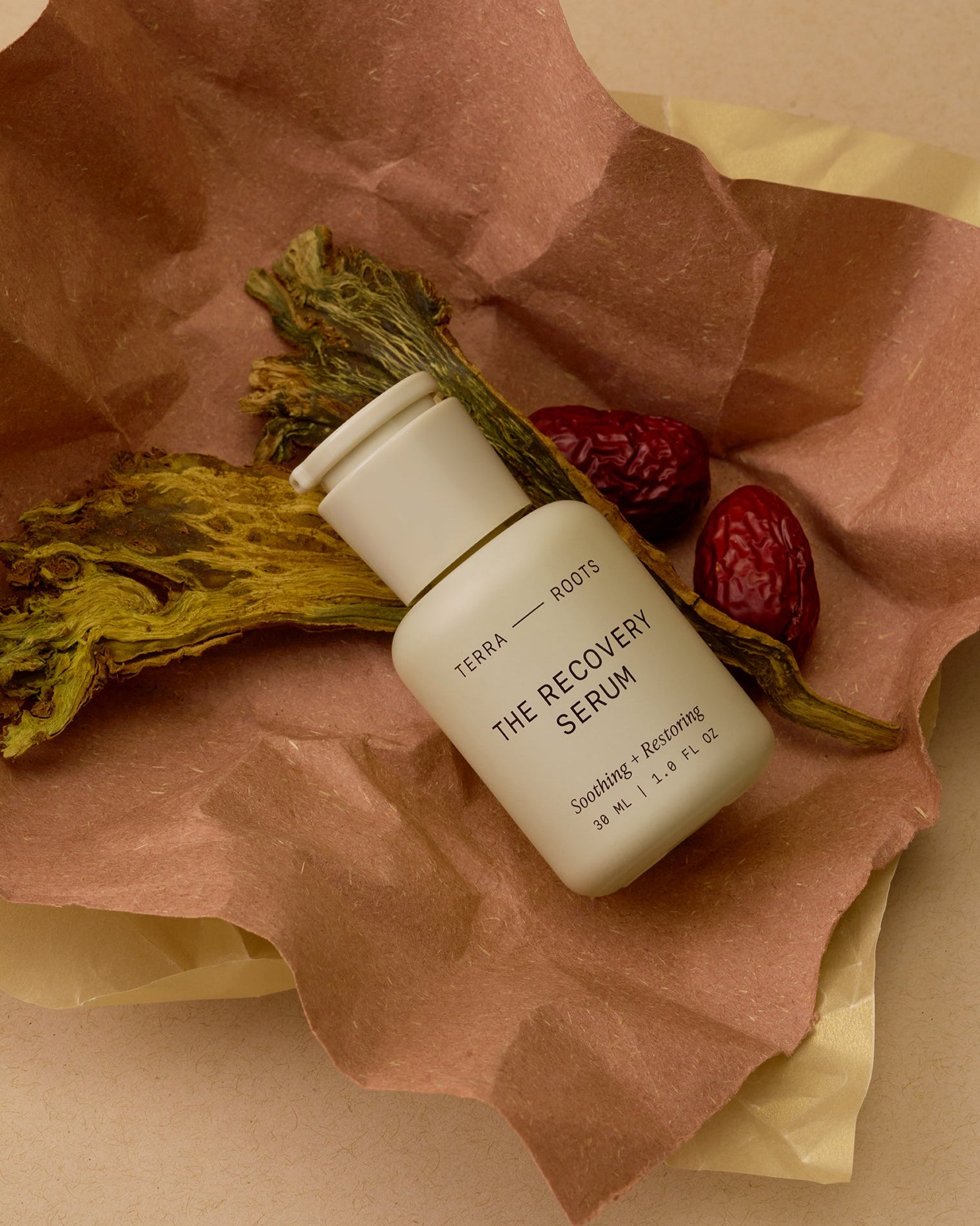 Terra Roots The Recovery Serum bottle on brown paper with dried herbs