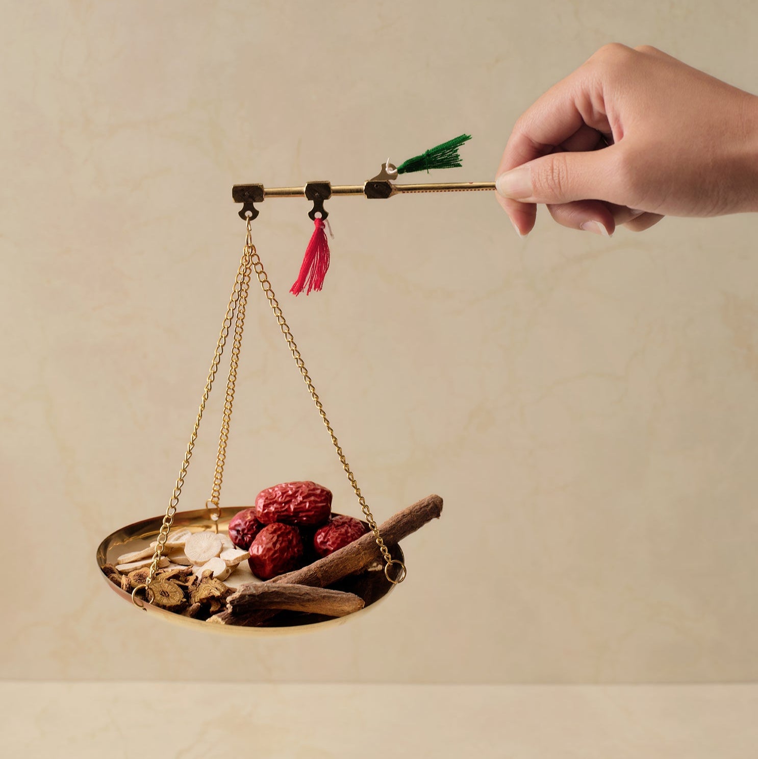Hand holding a traditional Chinese medicine scale with herbs on a beige background