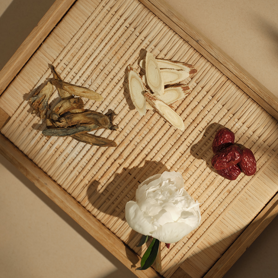 Herbal ingredients including dried roots, slices of ginseng, and red dates on a woven mat.