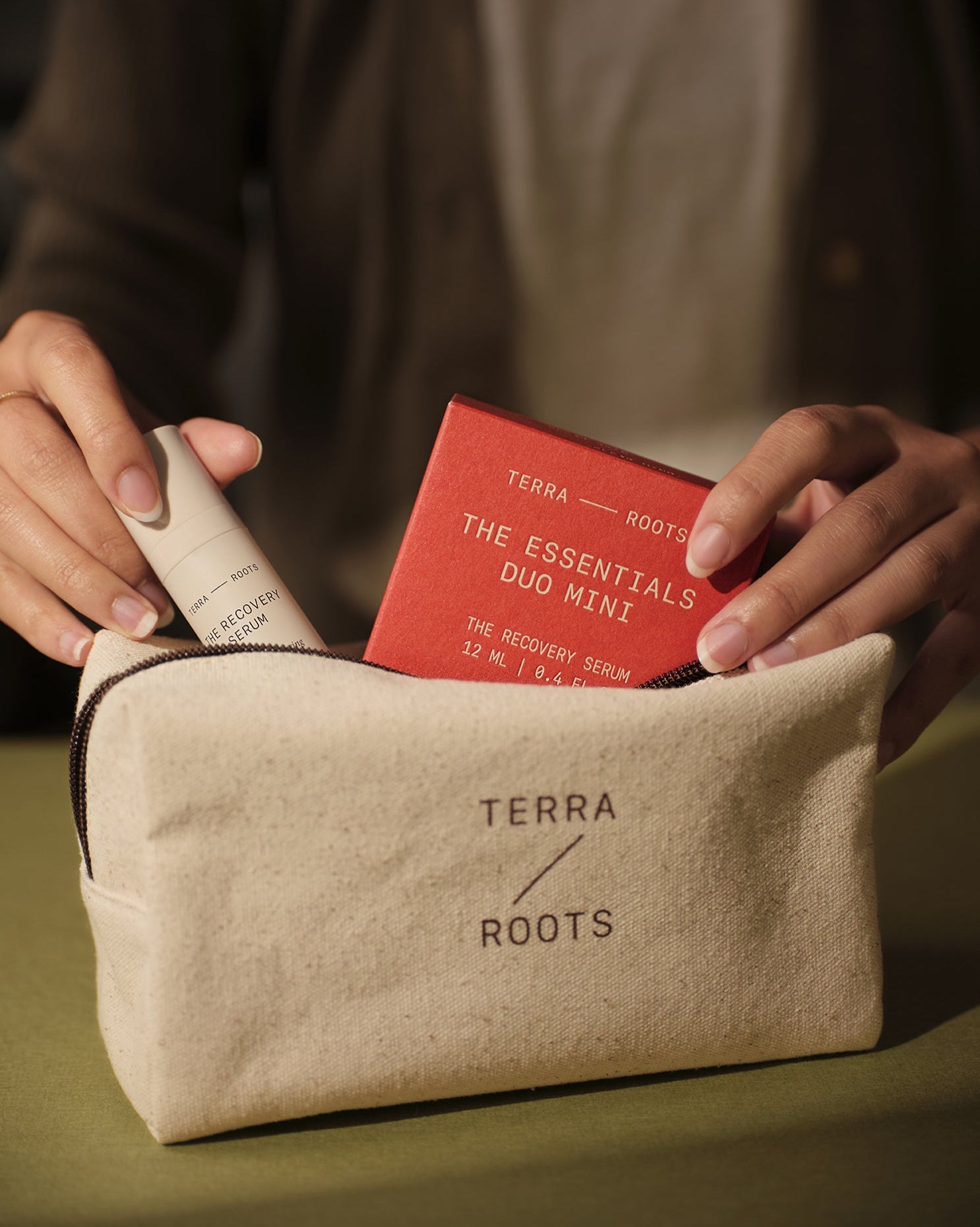 Person holding a Terra Roots pouch with skincare products on a green background